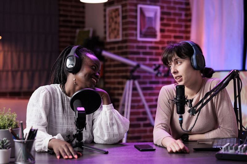 Two podcast co-hosts talking at microphones in a neon-lit studio.