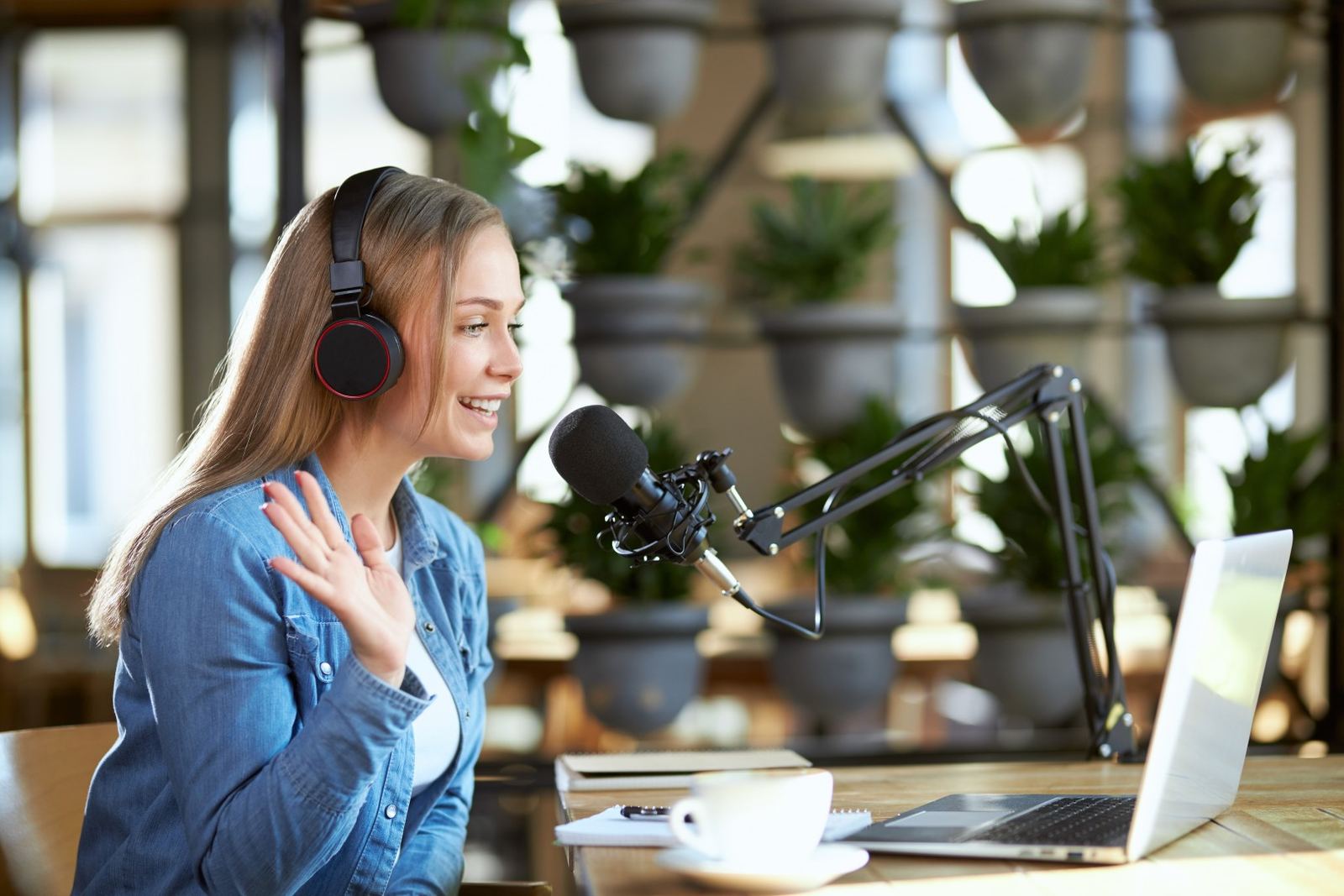 A presenter speaking into a studio microphone at a desk, with a laptop beside her.