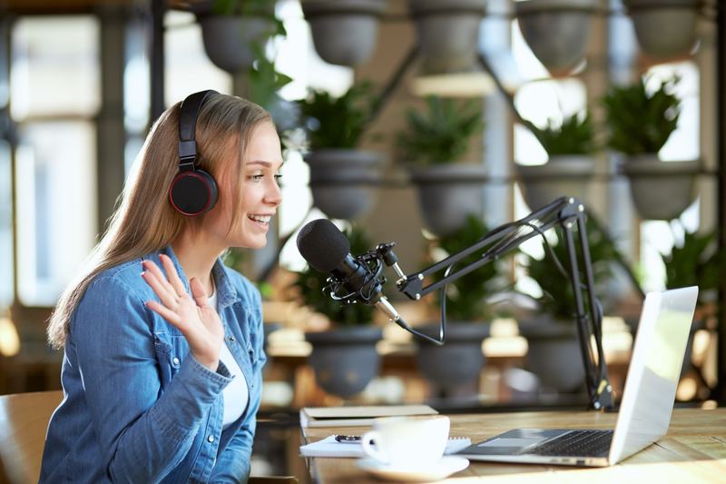 A presenter speaking into a studio microphone beside a laptop.