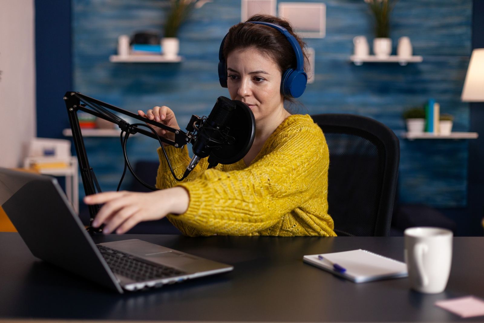 A podcaster in a home studio speaking into a broadcast microphone with a headset on.